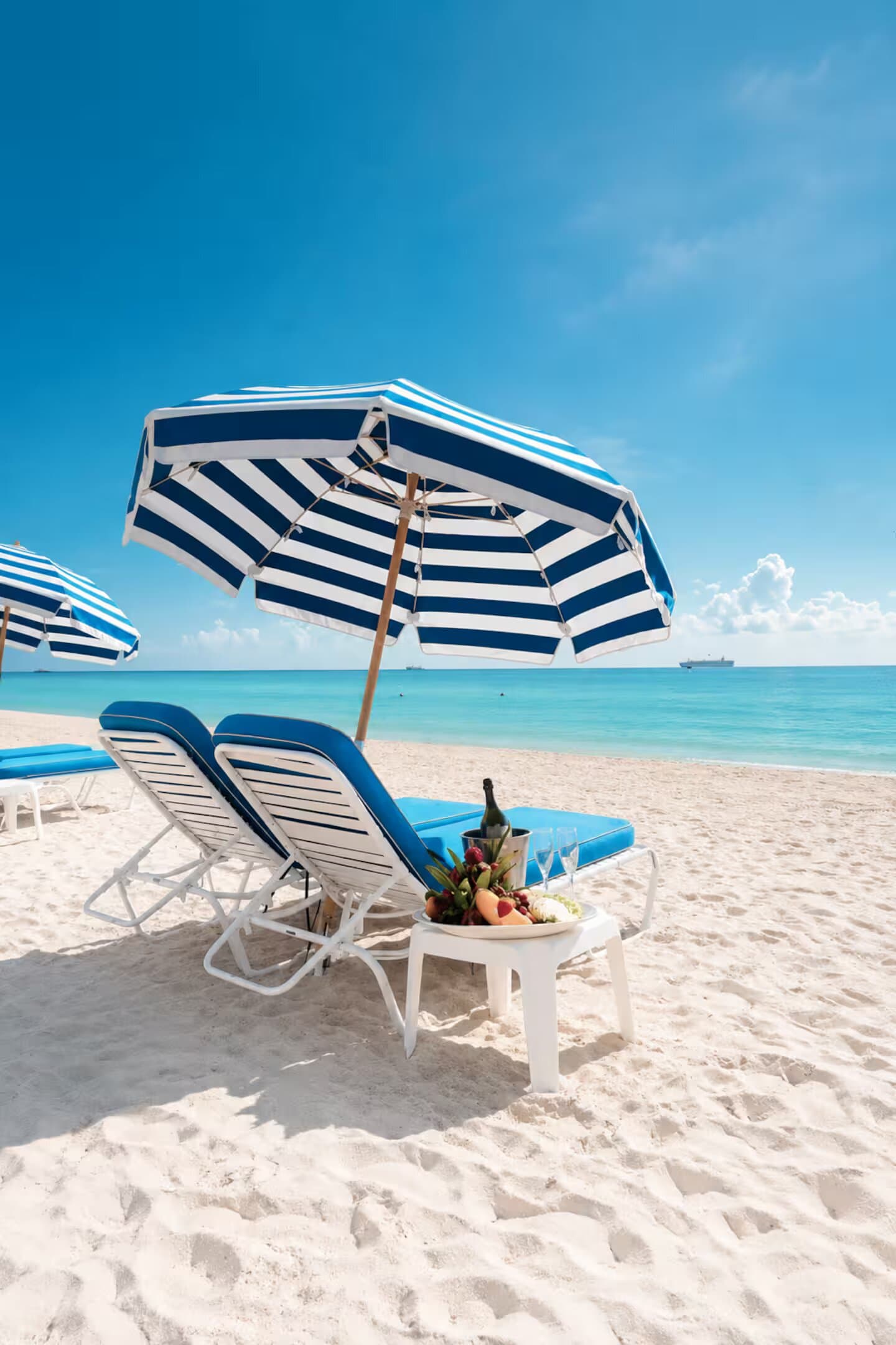 Two beach chairs and a striped umbrella set on the sand at the Bentley Beach Club