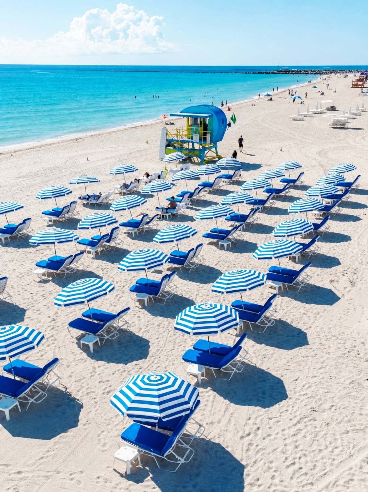 Rows of blue-striped umbrellas and loungers on South Beach at the Bentley Beach Club, lifeguard tower behind